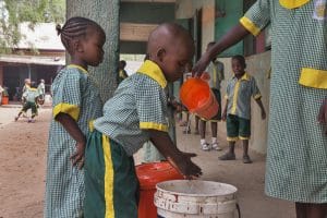 On 17 March 2015, (left-right) a young girl waits her turn while a boy washes his hands with water that an older girl is pouring from a pitcher, after lunch at St Theresa Catholic School in Yola, capital of the north-eastern state of Adamawa, which has been affected by the escalating Boko Haram insurgency. The school is hosting students whose families have been displaced by the armed conflict. In March 2015 in Nigeria, 15.5 million people, including 7.3 million children, are affected by the continuing crisis in the countrys north-eastern region. More than 1.2 million Nigerians have fled their homes as a result of violence and attacks by Boko Haram insurgents that have escalated since the beginning of 2015. Many of the displaced, most of whom are children and women, are sheltering with in host communities that have limited resources, and in formal and informal camps. All are in urgent need basic supplies, health and nutrition services, and critical water sanitation and hygiene support to prevent the spread of disease. Over 150,000 people, the vast majority children and women  have also fled to neighbouring Cameroon, Chad and Niger, further straining vulnerable communities  some of which are already facing food insecurity and malnutrition, are prone to disease outbreaks and natural disasters, and often already host hundreds of thousands of refugees, returnees and migrants who have escaped violence and hardship throughout the region. The impact of the crisis on children and women is of particular concern. Many of them have lost their homes and belongings escaping with only the clothing they were wearing; and some have walked for days  or even weeks  to find refuge. Many children in the region have been traumatized and are in need of psychosocial support. They have witnessed violence and atrocities, including seeing parents and siblings slaughtered by Boko Haram insurgents; and have been exposed to or have experienced violence and brutality. Thei